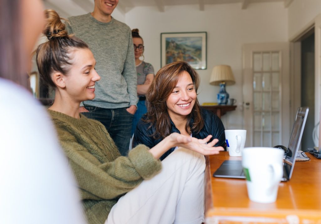 Image shows 4 people in shot, one wearing a green top and another wearing a dark top smiling off shot