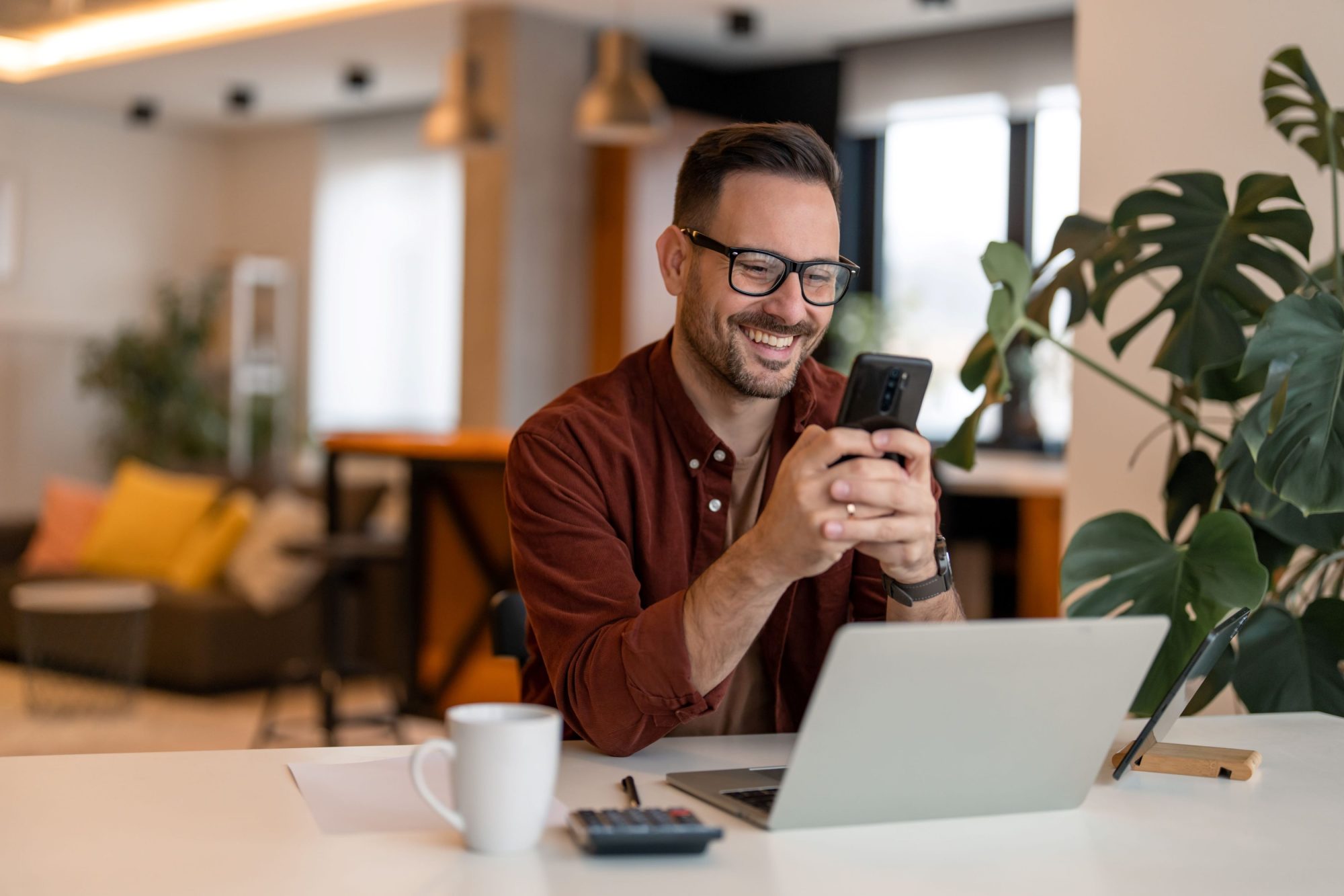 Individual sitting working in a cafe, looking at his investments on his phone and smiling