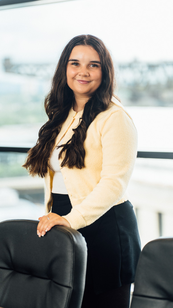 An image of Iona Duff standing in the Edinburgh office and wearing a yellow cardigan.