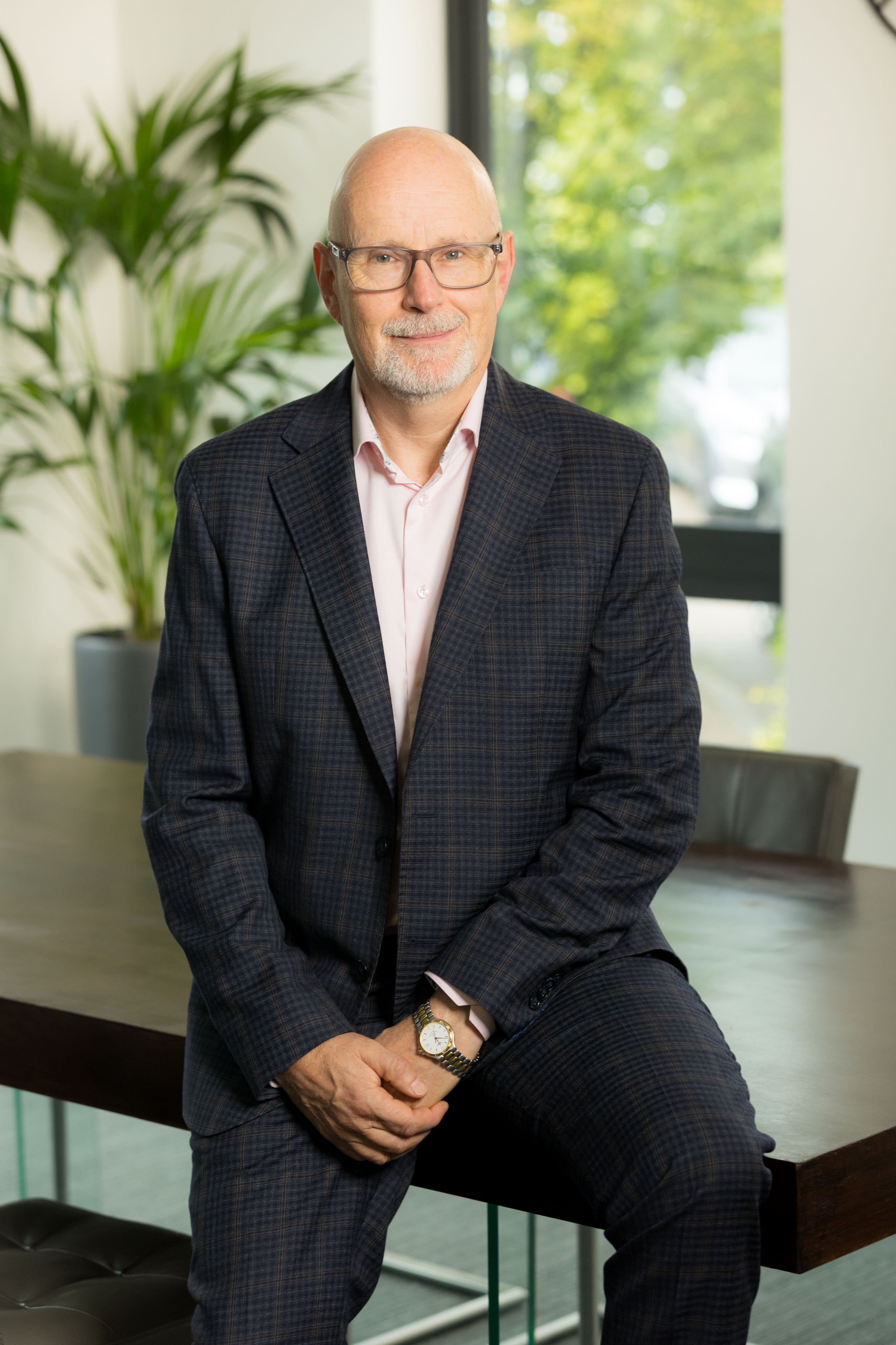 An image of Michael Aitken leaning on a table with his hands crossed.