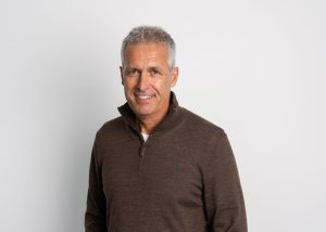 An image of Glen Brophy wearing a brown jumper and smiling at the camera.