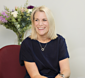 Nicola Watts, Partner, AAB Wealth sat on a burgundy chair with a bouquet of white and purple flowers