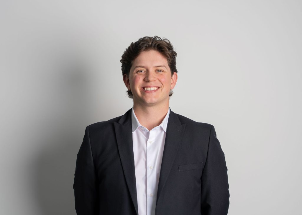 An image of Fintan McKenna wearing a white shirt and blazer. He is smiling at the camera.
